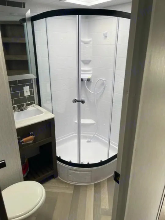 Inside an RV rental bathroom: a clear-door corner shower, dark wood vanity with sink, and toilet, all designed for compact living.. salem 29VBUD 2022