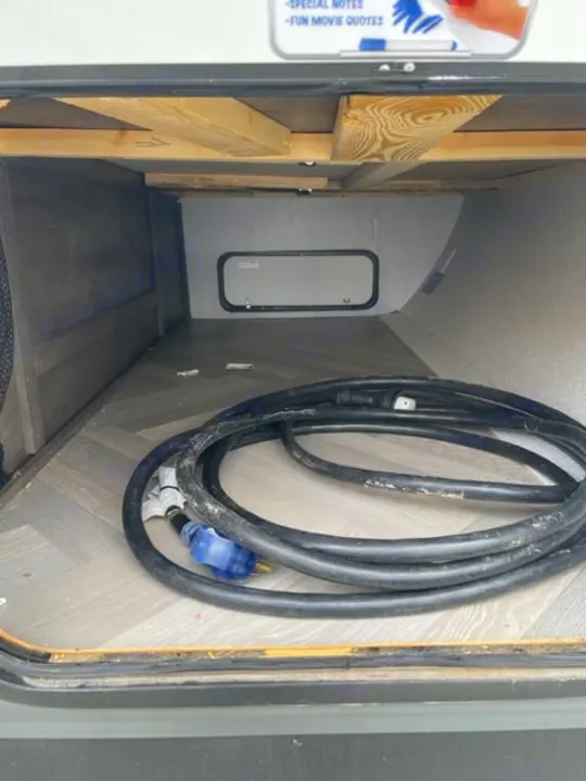 Inside an RV rental's under-bed storage area, a coiled power cord lies on the floor, framed by wooden supports.. salem 29VBUD 2022