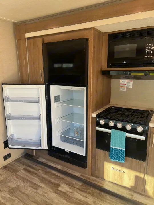 RV rental kitchen showcasing an open refrigerator, microwave, and stove/oven. Clean, practical space for your journey.. Grand Design Imagine XLS 2023