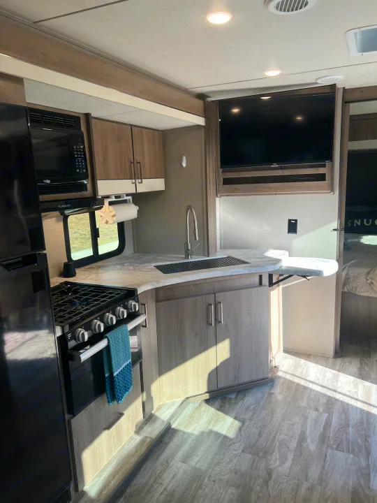 Experience comfort in this RV rental with a well-equipped kitchen featuring a stove, microwave, sink, and smart TV.. Grand Design Imagine XLS 2023