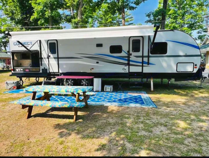 Spacious RV rental set up for comfortable camping, featuring an outdoor kitchen, picnic tables, and area rugs.. KZ Connect 2019