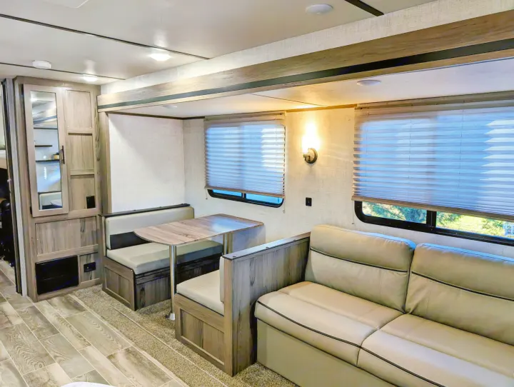 Experience comfort in this RV rental interior! Features a welcoming dinette and cozy sofa, with warm lighting and ample windows.. Gulf Stream Ameri-Lite 2022
