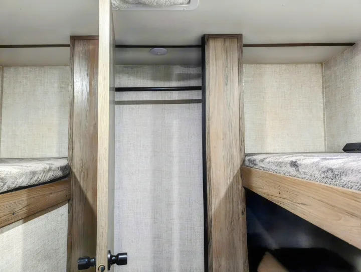 RV rental interior: cozy bunk beds flank a central closet with a hanging rod. Light wood and textured walls.. Gulf Stream Ameri-Lite 2022