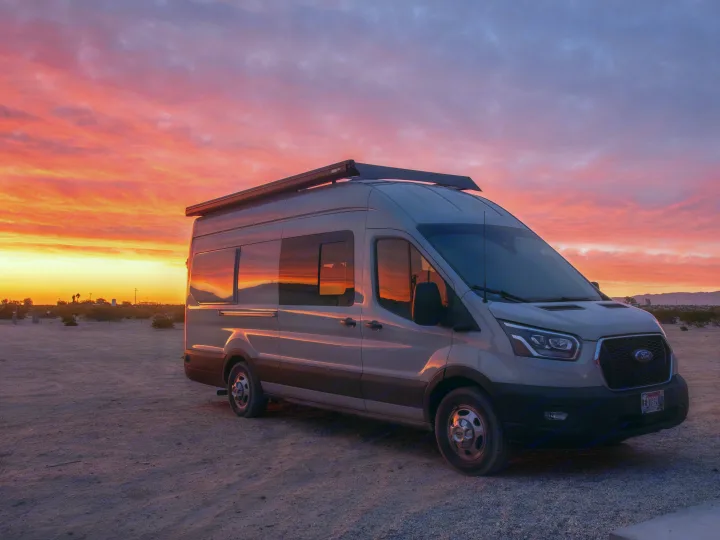 An RV rental camper van bathed in the vibrant hues of a desert sunset. Perfect for adventure!. Ford Transit 2022