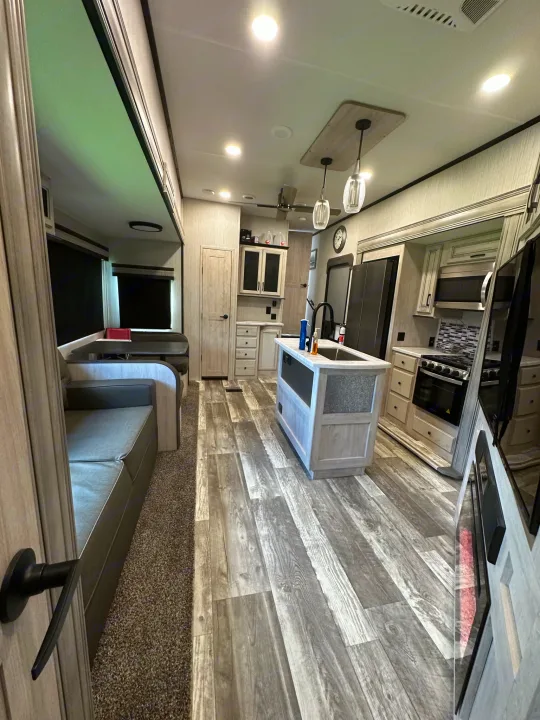 Spacious, modern RV rental interior featuring a kitchen island, dining booth, and sofa with wood-look flooring.. Forest River Sierra 2022