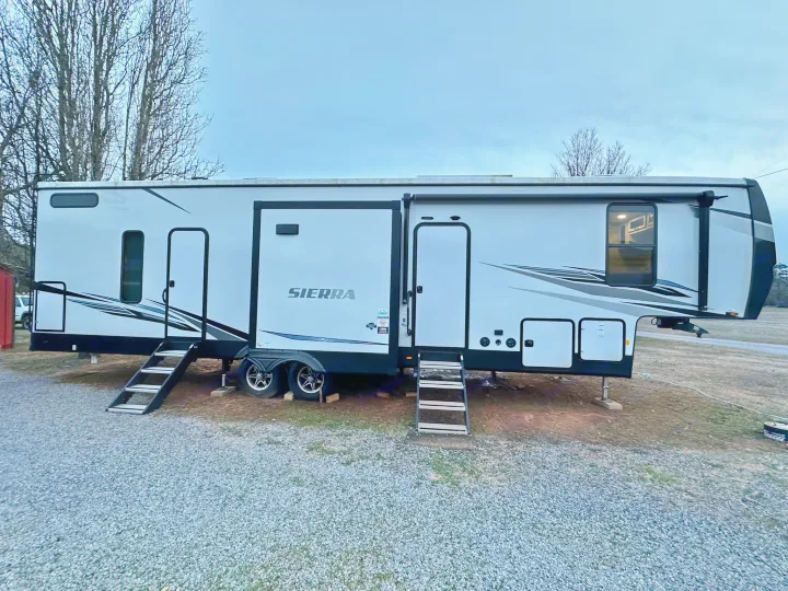 This white Sierra fifth-wheel RV rental, with extended slide-outs, is parked on gravel, ready for travel.. Forest River Sierra 2022