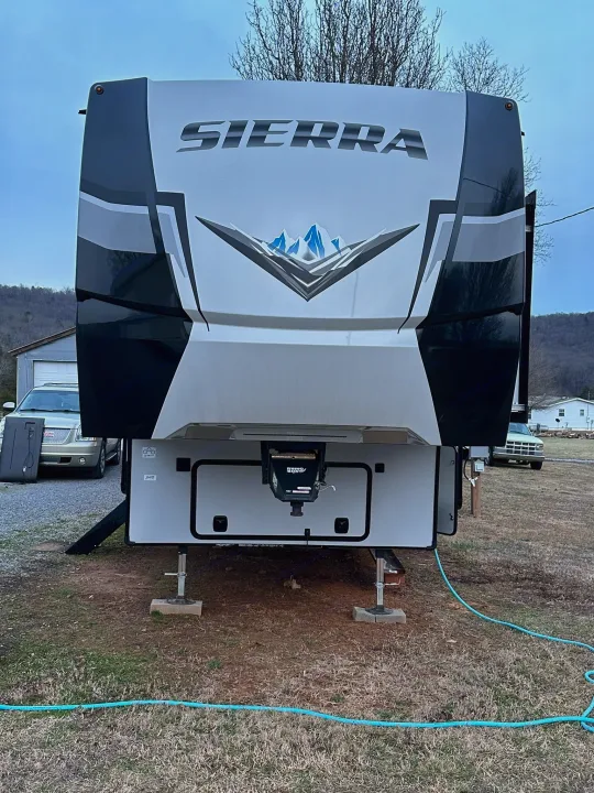 White and black Sierra fifth-wheel RV, ready for your next rv rental trip. This large recreational vehicle is parked and leveled on a grassy site.. Forest River Sierra 2022