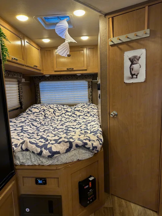 View inside a modern RV rental, featuring a comfortable bedroom with a patterned duvet, wood cabinets, and power controls.. Thor Four Winds 2019