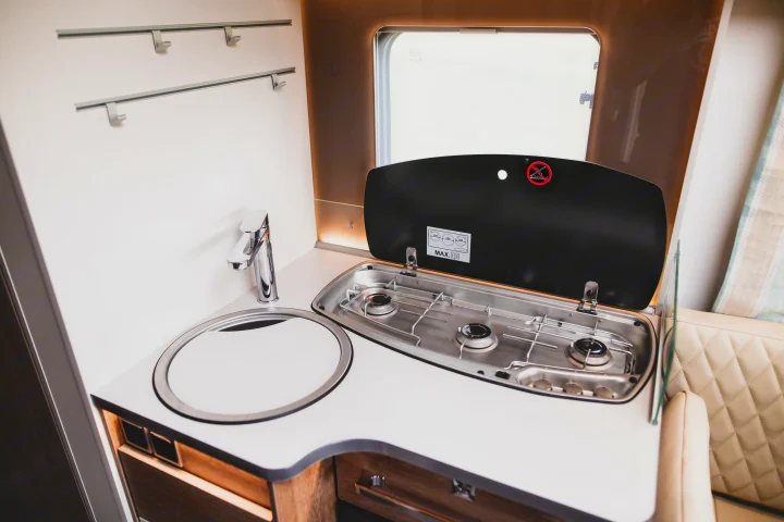 Compact kitchen in an RV rental, with a sink, modern faucet, and an open three-burner gas stove for convenient cooking.. GlamperRV DBL 2026
