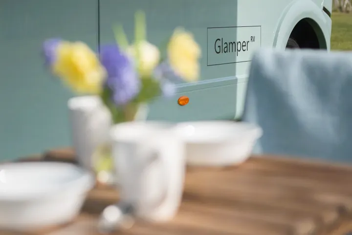 Outdoor dining setup with flowers next to a teal Glamper RV. Ideal for your next rv rental adventure.. GlamperRV DBL 2026