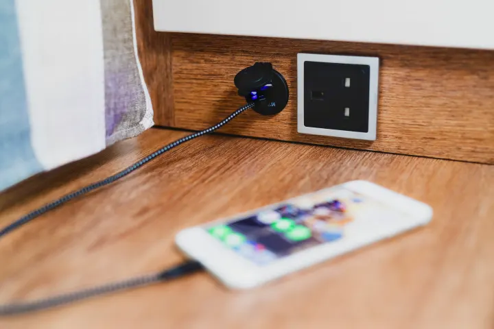 Smartphone charging in an RV rental: a phone connected to a built-in USB port (glowing blue) next to an electrical outlet.. GlamperRV DBM Automatic 2025