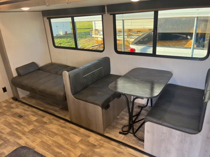 Spacious RV rental interior: a comfortable dinette with table and benches, plus a convertible sofa bed.. Dutchmen Kodiak Bunk House 2019
