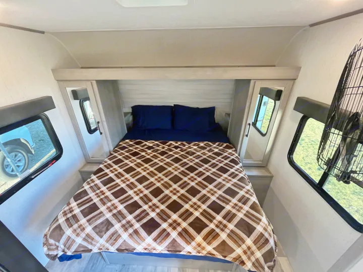 Cozy RV rental bedroom featuring a comfy plaid-covered bed, overhead cabinets, and windows revealing outdoor views.. Dutchmen Kodiak Bunk House 2019