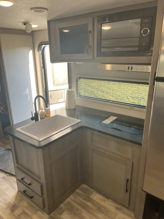 Modern RV rental kitchen with sink, microwave, and cooktop. Bright interior with light wood cabinetry and counter.. Dutchmen Kodiak Bunk House 2019