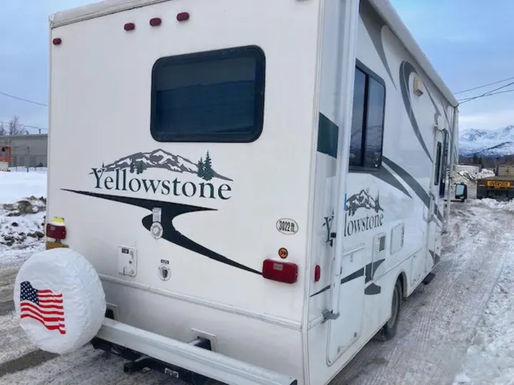 Rear and side view of a white Yellowstone RV rental. Parked in snow, it features an American flag spare tire cover.. Yellowstone Conquest M6254 2008