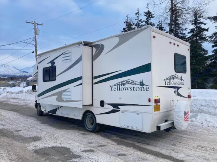 A white Yellowstone RV rental is parked on a snowy road with its slide-out extended, mountains in the distance.. Yellowstone Conquest M6254 2008