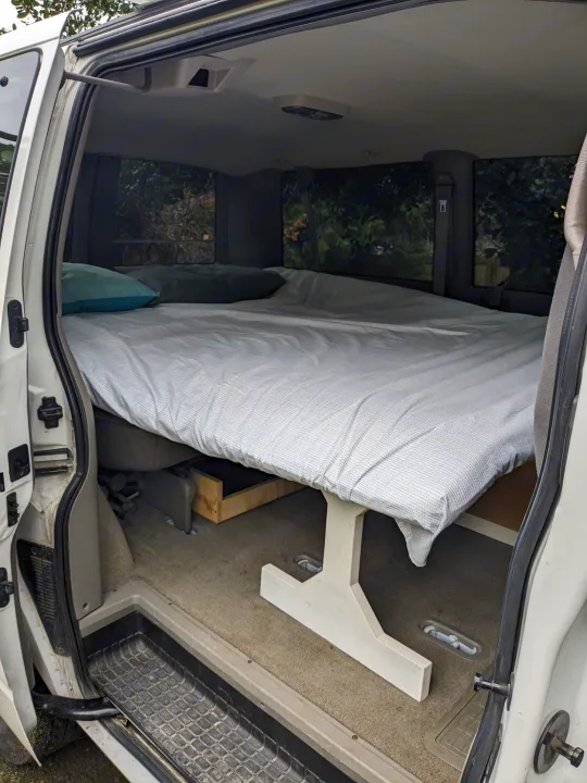 Interior of an RV rental van conversion featuring a large bed with pillows, elevated for storage, ready for camping.. Chevrolet Open Road 2002