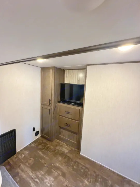 RV rental interior features: built-in TV, wood-look flooring, white walls, and modern dark wood storage.. Forest River Sabre 2021