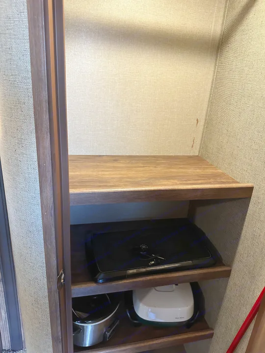 This RV rental cabinet features wooden shelves and fabric walls. A griddle, slow cooker, and other appliances are stored inside.. Keystone RV Cougar 2019
