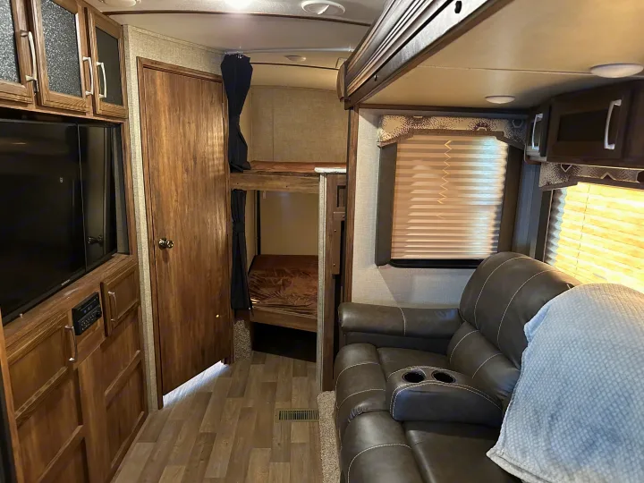 Inside an rv rental: cozy living space with a large TV, plush recliner, and built-in bunk beds.. Keystone RV Cougar 2019
