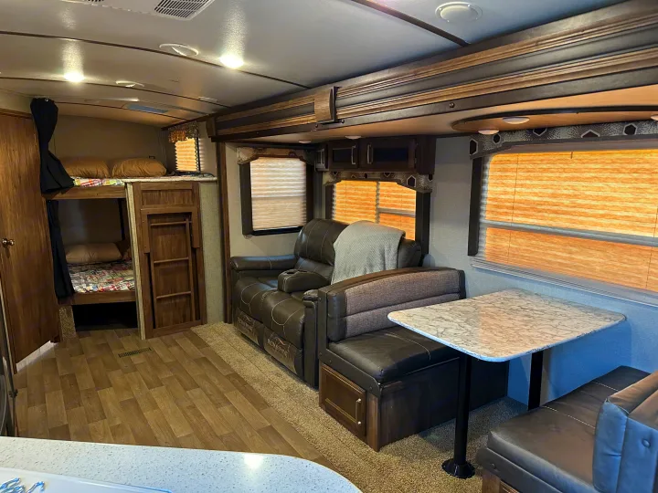Spacious RV rental interior featuring bunk beds, recliners, and a cozy dinette setup.. Keystone RV Cougar 2019