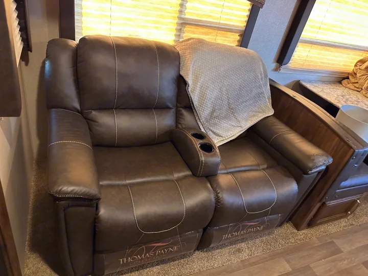 Cozy brown faux leather reclining loveseat with cup holders, perfect for relaxing in an RV rental interior.. Keystone RV Cougar 2019