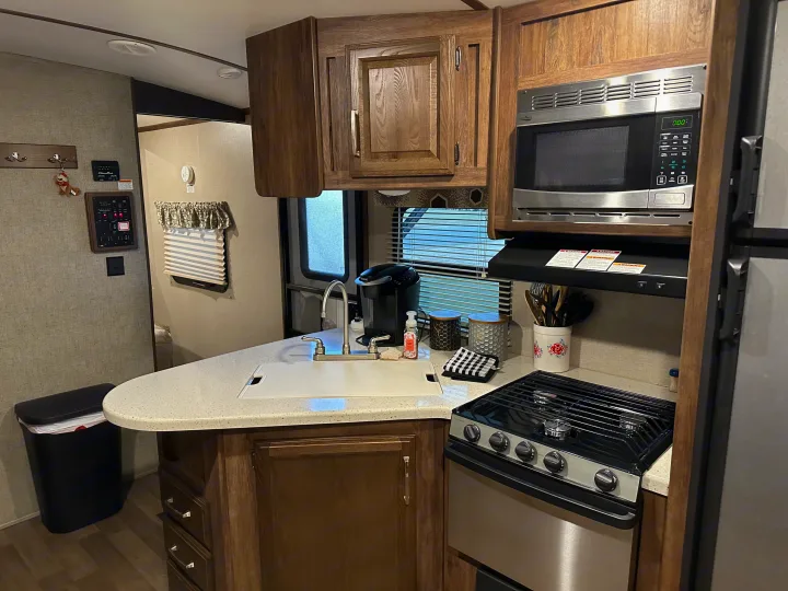RV rental kitchen with sink, stove, microwave, and coffee maker, showing compact yet functional amenities.. Keystone RV Cougar 2019
