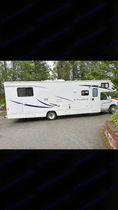 White RV rental motorhome parked on an asphalt driveway, with green trees in the background.. Winnebago Chalet 2010