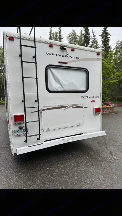 Wet, white Winnebago Chalet RV (motorhome) from the rear, featuring a ladder & Alaska plate. Ideal for an RV rental adventure.. Winnebago Chalet 2010