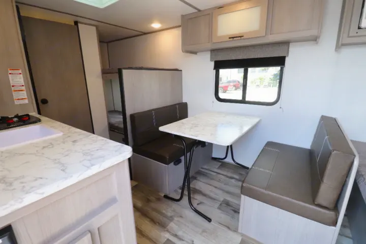 RV rental interior: kitchen with sink & marble-look counter, dining booth, and bunk beds in light wood finish.. Coleman LT17B 2024