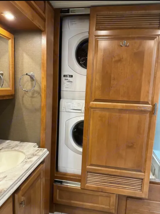 Compact RV rental showing a stacked washer and dryer laundry unit, visible behind a partially open wooden door.. Tiffin Motorhomes Phaeton 2019