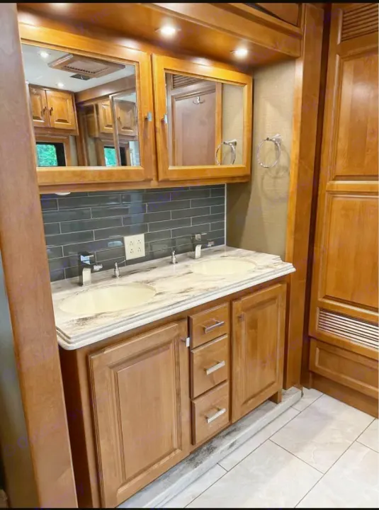 Spacious RV rental bathroom featuring a modern dual-sink vanity, wood cabinetry, and sleek backsplash.. Tiffin Motorhomes Phaeton 2019
