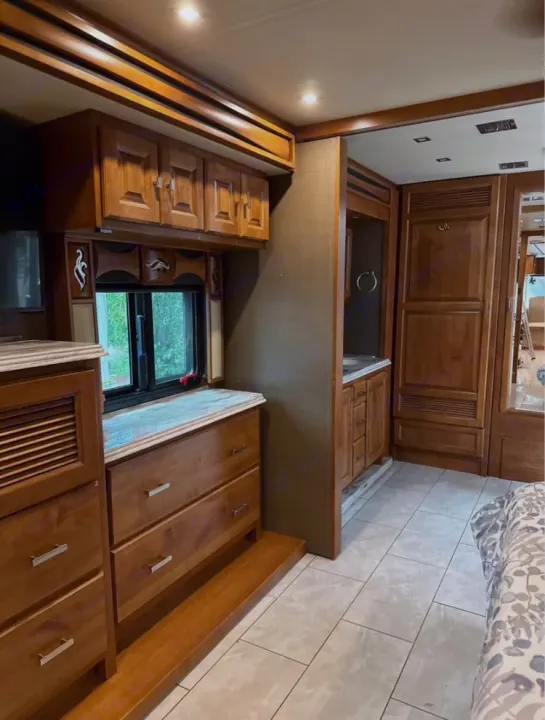 Luxury RV rental bedroom suite featuring wood cabinets, dresser, tiled floor, and a connecting private vanity area.. Tiffin Motorhomes Phaeton 2019