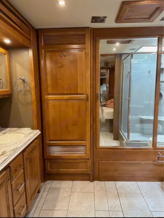 Spacious RV rental interior with wood cabinetry. Bathroom vanity, pantry, mirrored door to bedroom & shower. Tiled floor.. Tiffin Motorhomes Phaeton 2019