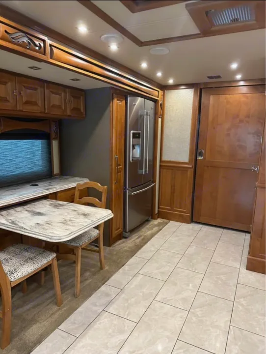 Clean RV rental interior: compact kitchen, dining table, large fridge, and warm wood finishes throughout.. Tiffin Motorhomes Phaeton 2019