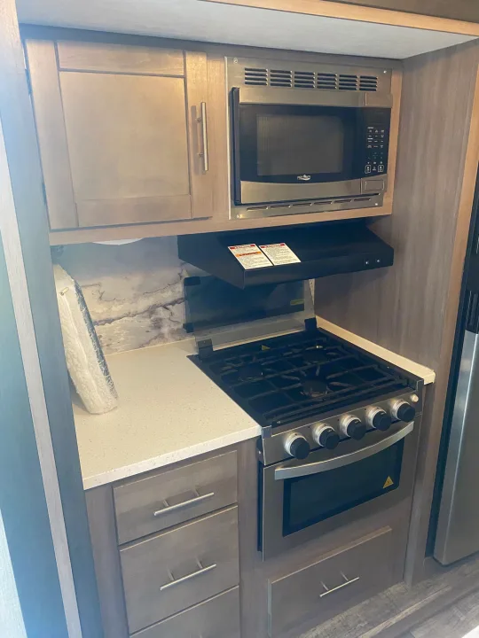 RV rental kitchen features: microwave, gas stove, oven, range hood, cabinets, and bright countertop. Everything you need!. Crossroads RV Sunset Trail 2022