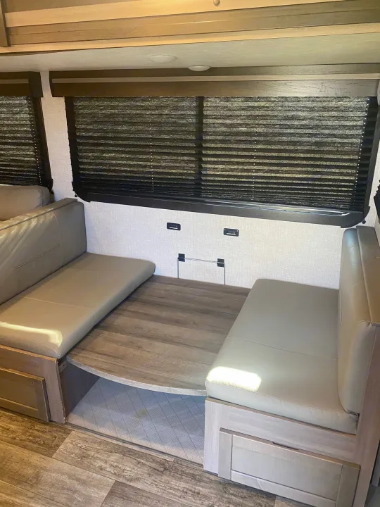 RV rental interior: modern dinette with upholstered bench seating, wooden table, and dark window blinds.. Crossroads RV Sunset Trail 2022