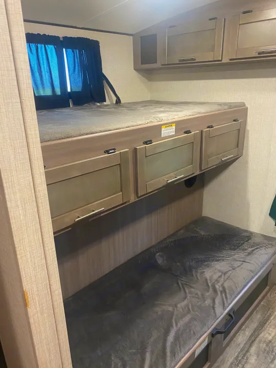 Cozy RV rental bunk beds with window & storage. Perfect for family trips, offering comfortable sleeping arrangements.. Crossroads RV Sunset Trail 2022