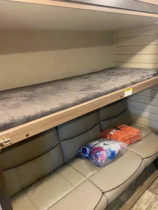 RV rental interior showing a cozy bunk bed above a light-colored sofa with bundled bedding.. Crossroads RV Sunset Trail 2022