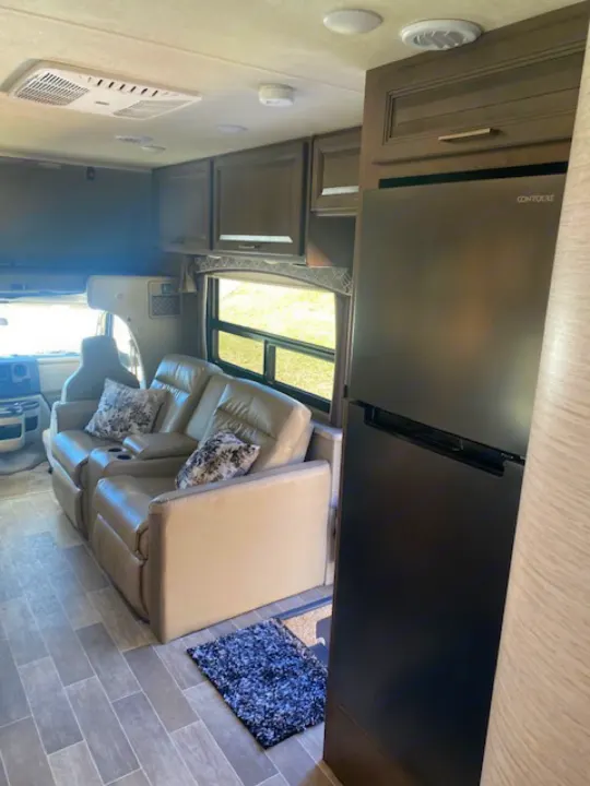 RV rental interior featuring plush recliners, a large black refrigerator, and overhead cabinets in a cozy living space.. Thor Chateau 2021
