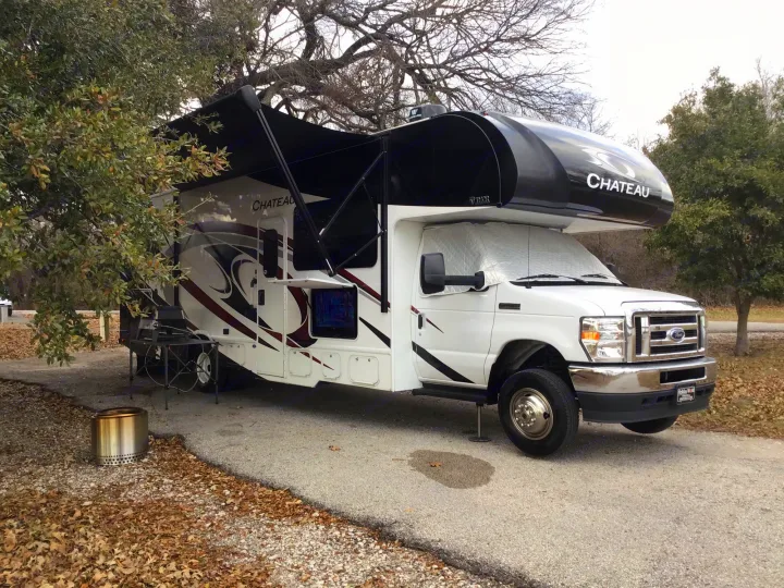 Spacious Chateau RV rental at a scenic campsite. Features an extended awning, outdoor grill, and fire pit.. Thor Chateau 2021