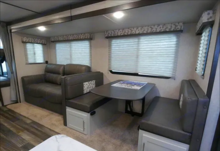 RV rental's inviting interior: featuring a cozy sofa and practical dinette with seating, ideal for road trips.. Keystone Bullet 2021