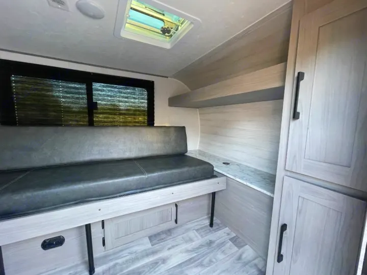 Inside a compact RV rental: gray bench seating, light wood-look interior, storage cabinets, and skylight.. Dutchmen Coleman Rubicon 2023