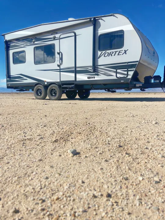 This grey Vortex RV rental travel trailer is ready for adventure, parked on a gravel plain under a clear blue sky.. Genesis Supreme Rv Genesis Supreme 2022