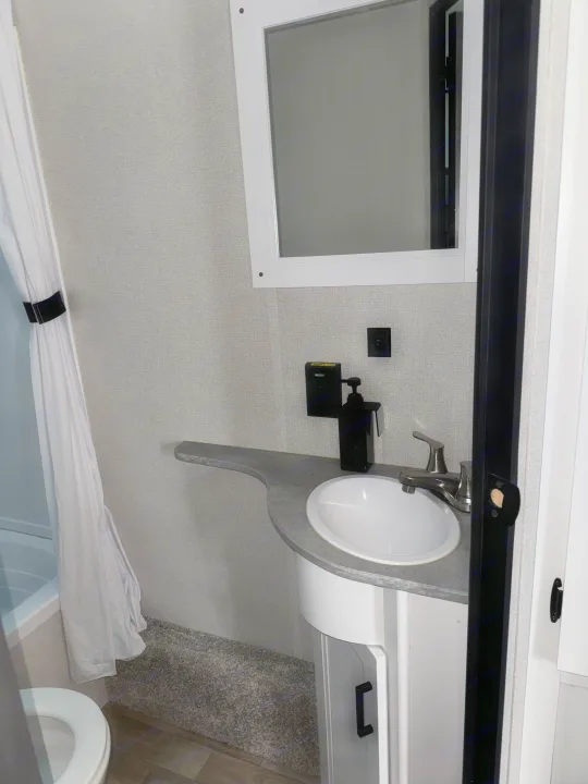 Compact RV rental bathroom with modern vanity, sink, mirror, and shower, offering comfort on the go.. Keystone Hideout 2022