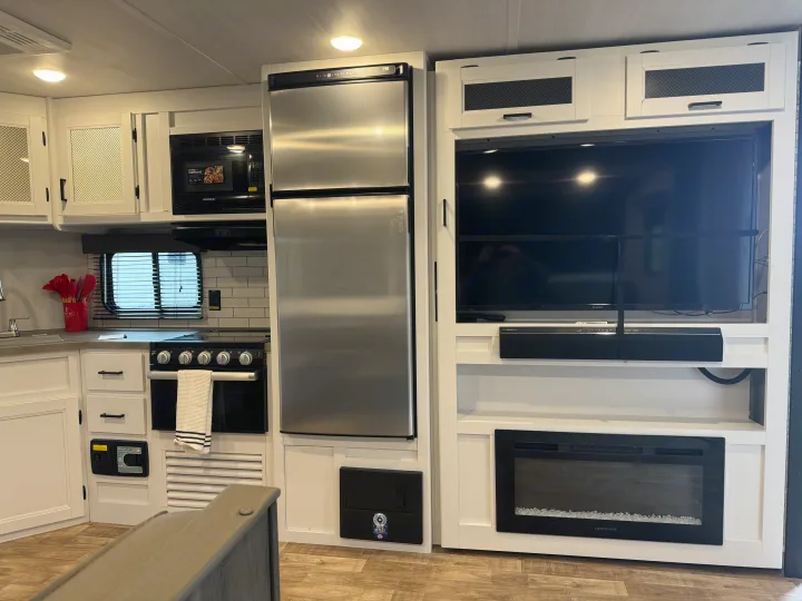 Modern RV rental kitchen & living space. Features include fridge, stove, microwave, TV, and electric fireplace.. keystone hideout 2022