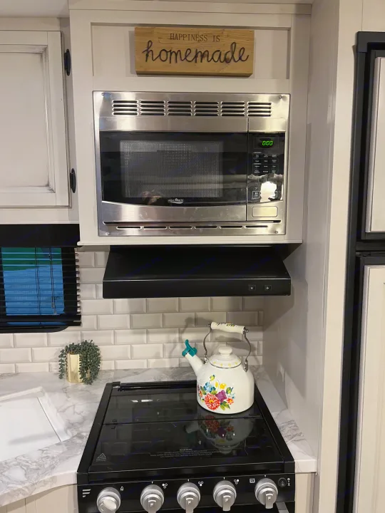 Modern RV rental kitchen with microwave, stovetop, white subway tile, and a "Happiness is Homemade" sign.. Jayco Jay Flight 2022