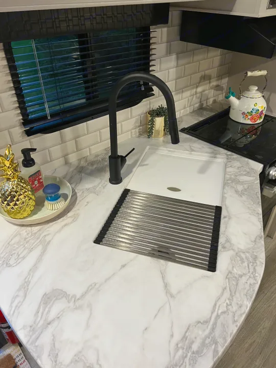 Organized RV rental kitchen: white marble-look counters, black faucet, sink with drying rack, subway tile, and floral kettle on stovetop.. Jayco Jay Flight 2022