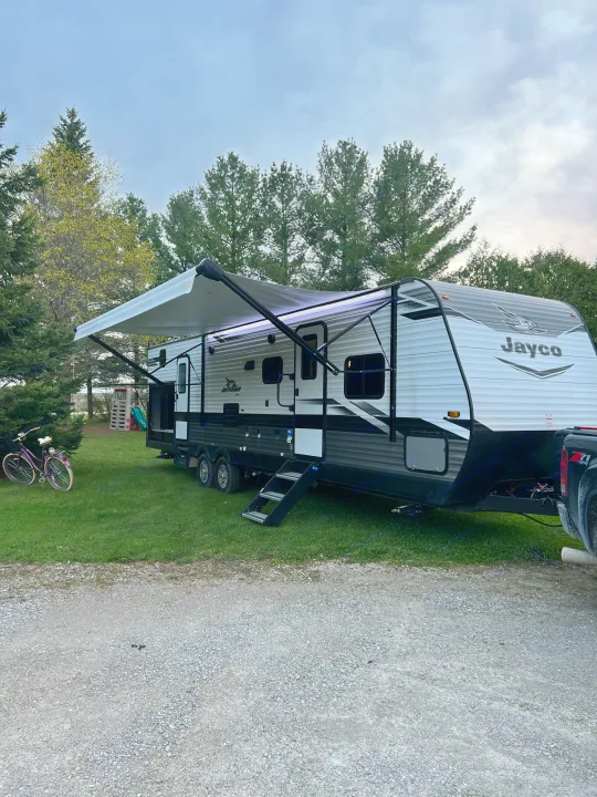 Jayco travel trailer RV rental parked at a grassy campsite. Awning extended with lights, purple bike nearby.. Jayco Jay Flight 2022