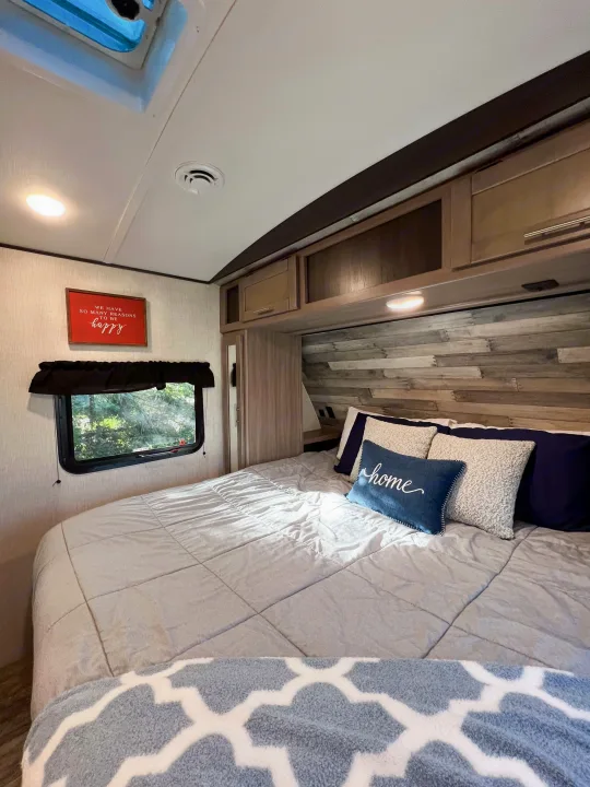 This cozy RV rental bedroom features a comfy bed, wood-paneled headboard, overhead storage, and natural light.. Crossroads RV Sunset Trail Super Lite 2022